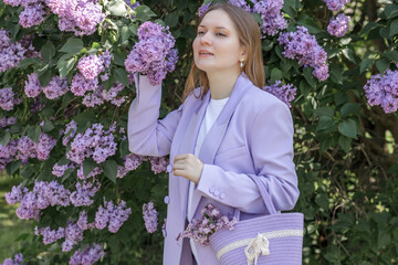 A beautiful young blonde woman, against a background of blooming lilacs, in a lilac trouser suit....