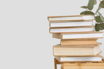Stack of books and eucalyptus branches on table near white wall, closeup