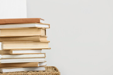 Stack of books on wicker basket near white wall