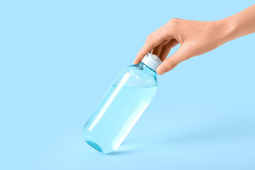 Female hand with bottle of micellar water on blue background, closeup