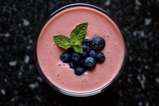 Fresh smoothie topped with blueberries and mint on dark surface