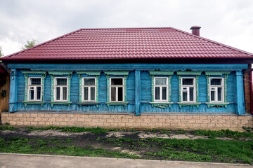 Old wood Russian house with carved windows (architraves). Building on stone foundation, windows on long side along street. But modern metal-tile. Central Russia. 19th century provincial houses