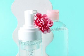 Bottles of micellar water, carnation flower and plaster stand on turquoise background, closeup