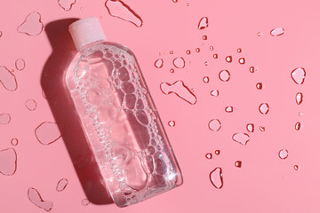 Bottle of micellar water and water drops on pink background, closeup