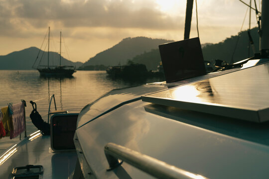 scenic view of morning calm tranquil sunrise from the boat deck at anchor stop, rising sun, mountains, sea with light reflections, twilight colors, sailing boats, serene harbour