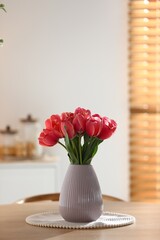 Beautiful tulips in vase on wooden table indoors. Space for text