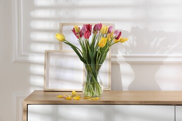 Bouquet of beautiful tulips and frames on wooden table indoors
