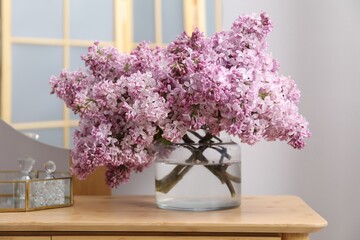 Beautiful lilac flowers in glass vase and perfumes on wooden table indoors