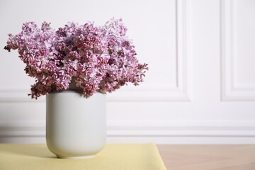 Beautiful lilac flowers in vase on table near white wall indoors, space for text