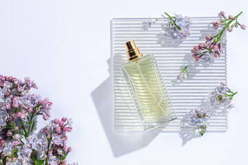 Bottle of perfume and beautiful lilac flowers on white background, flat lay