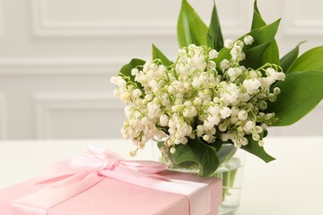 Beautiful lilies of the valley flowers and gift on white table, closeup