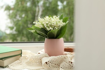 Bouquet of lily-of-the-valley flowers in vase and books on windowsill indoors