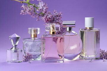 Bottles with perfumes and lilac flowers on purple gradient background, closeup