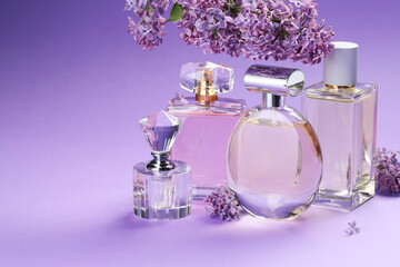 Bottles with perfumes and lilac flowers on purple gradient background, closeup. Space for text
