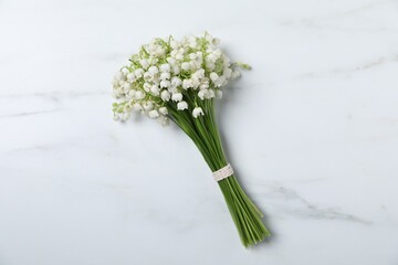Bouquet of beautiful lily-of-the-valley flowers on white marble background, top view
