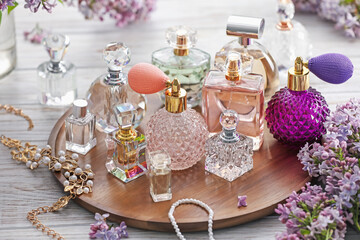 Bottles of perfumes, accessories and lilac flowers on white wooden table