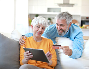 portrait of happy smiling senior elderly couple using a tablet computer and a credit card  for online shopping at home, technology and internet use in everyday life concept