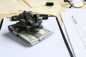 Money bonus. Dollar banknotes with bow, clipboard and checklist on table, closeup