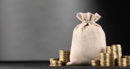 Bag and stacked coins on black table against gray gradient background, space for text