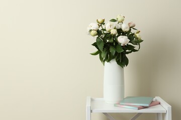 Bouquet of beautiful peony flowers in vase on shelving unit against beige background. Space for text