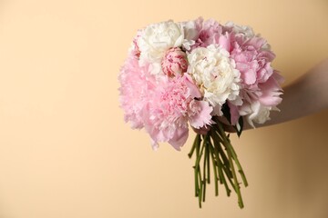 Woman holding bouquet of beautiful peonies on beige background, closeup. Space for text