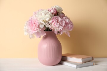 Beautiful peonies in vase and books on white table against beige background