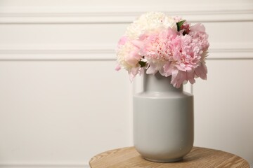 Beautiful peonies in vase on wooden table near white wall. Space for text