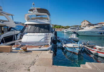 Several luxury yachts and boats are moored in a sunny marina with clear water, surrounded by calm...
