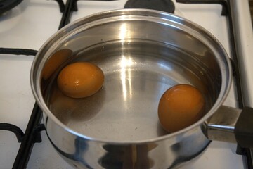 Two brown chicken eggs in the water in the cooking pan.
