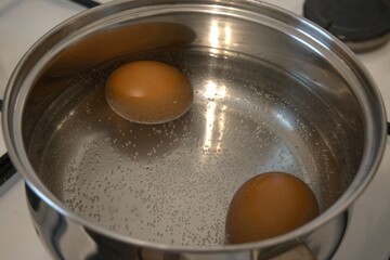 Two brown chicken eggs in the water in the cooking pan.