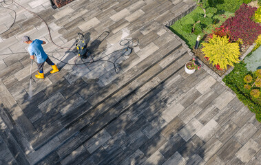 Worker Cleans Outdoor Patio With Pressure Washer During Sunny Day in Garden Area