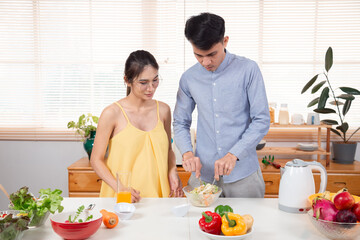 Beautiful pregnant mom and dad make healthy salad to eat together on weekend mornings. Young couple spending time together during cooking time. Family love healthy eating vegetable salad concept.