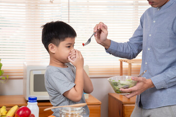 family activities lifestyles in kitchen, father try to encourage son to eat vegetable tomatoes in...