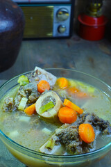 A warm bowl of Indonesian bone marrow soup with carrots and other vegetables, evoking a rustic, traditional Indonesian setting.