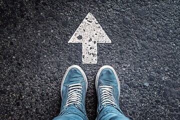 Top View of Sneakers and Painted Arrow Pointing Forward on Asphalt Road