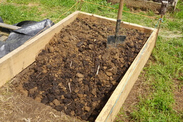 Gardener adding horse manure to raised garden bed with shovel