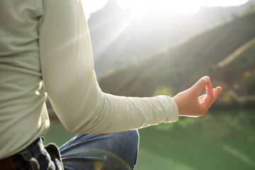 Woman doing yoga in nature mountain lake at sunset or sunrise background girl meditating practicing mindfulness holding hands in mudra gesture sitting in lotus pose feeling wellness, peace, energy zen