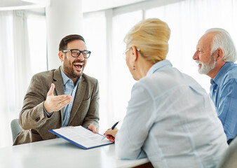 Portrait of a businessman or real estate agent or doctor shaking hands and signing a deal contract with senior couple in his office