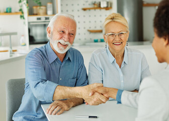 Portrait of a businessman or real estate agent or doctor shaking hands and signing a deal contract with senior couple in his office