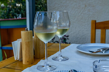 Two glasses of chilled white wine on an outdoor restaurant table with a white cloth. Soft evening light reflected in the glass. Relaxing summer ambiance.