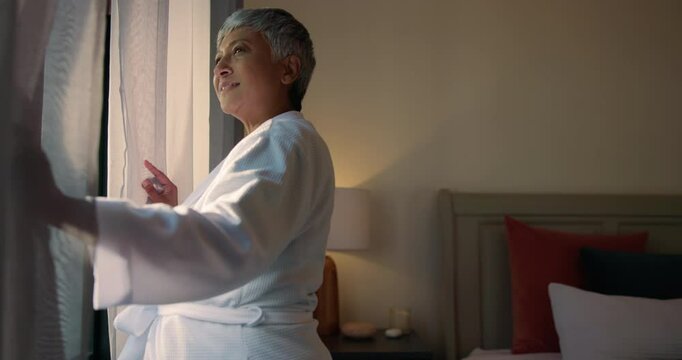Curtains, morning and wake up with old woman in hotel room for accommodation or hospitality. Retirement, smile and window with happy senior person at lodge or resort for holiday, travel and vacation