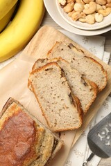 Cut banana bread with nuts, fruits and server on table, flat lay
