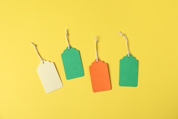 Blank tags with strings on yellow background, flat lay