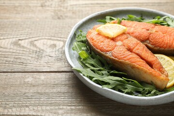 Seafood. Tasty salmon steaks, arugula and lemon on wooden table, closeup. Space for text