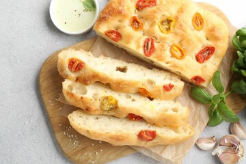 Cut delicious focaccia with tomatoes, spices and oil on gray table, flat lay