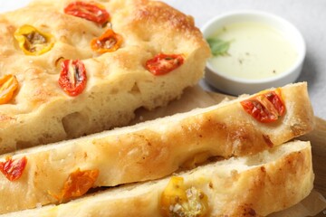 Cut delicious focaccia with tomatoes and oil on gray table, closeup