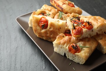Pieces of delicious focaccia with tomatoes and spices on gray textured table, closeup