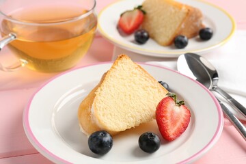 Pieces of tasty bundt cake with berries and tea on pink wooden table, closeup