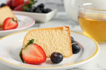 Piece of tasty bundt cake with berries and tea on white marble table, closeup