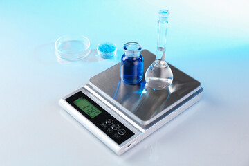 Scale with samples and laboratory glassware on white table in color lights, closeup